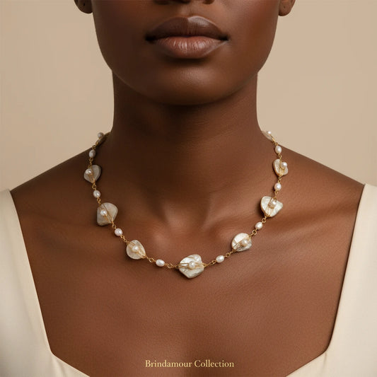 Elegant gold-plated necklace with organic shell leaf elements each holding a freshwater pearl on neutral background.